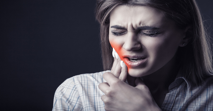 Young woman is suffering from a toothache against a dark background